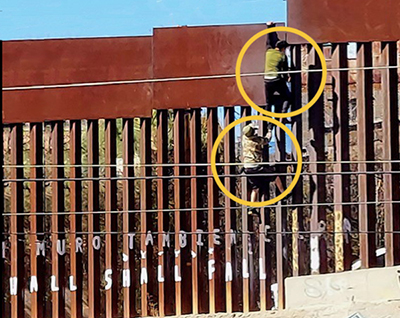 photo showing two immigrants scaling the border wall