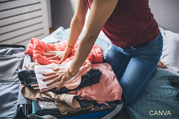 Photo of woman tring to cram clothes into overpacked suitcase